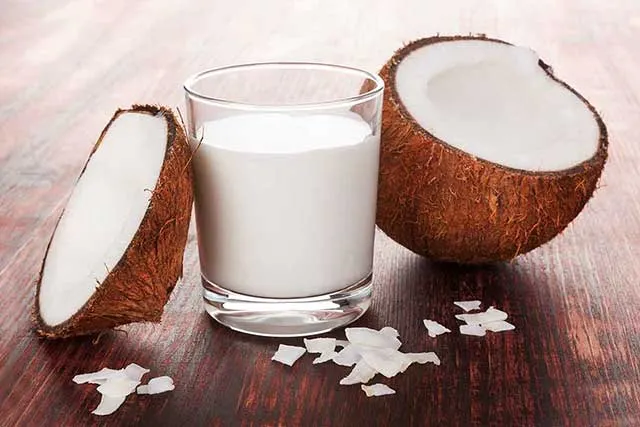 Un verre de crème de coco entre deux moitiés de noix de coco.